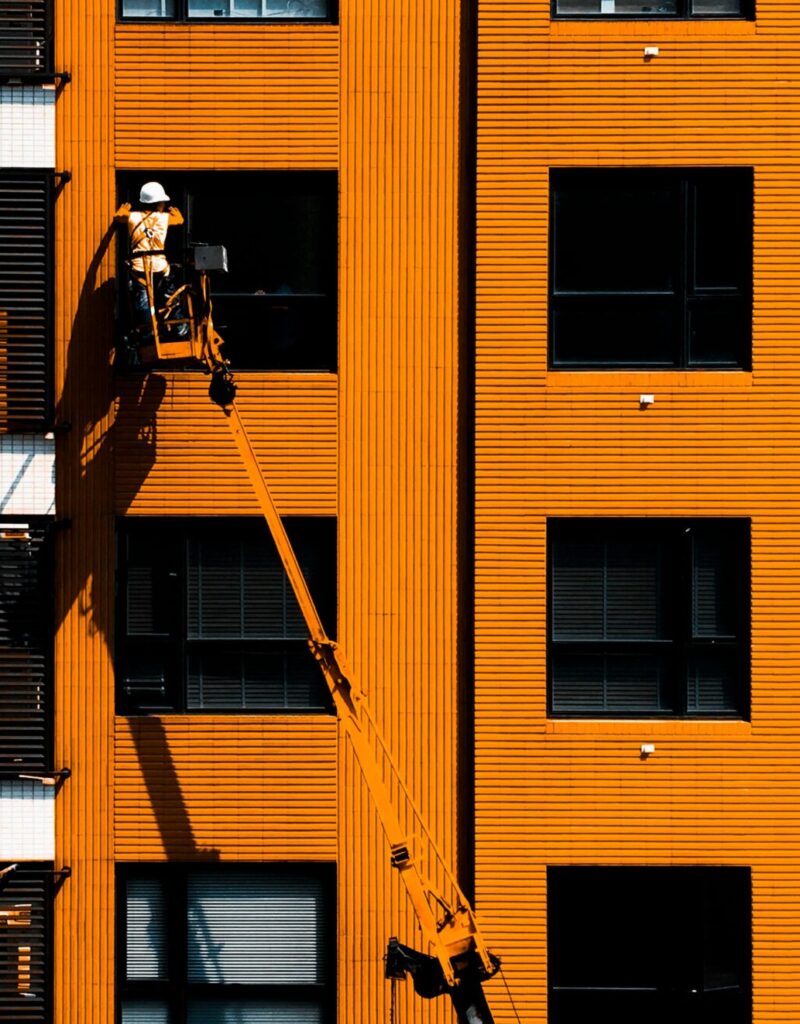 pexels-photo-2186572-2186572 A construction worker using a cherry picker working on an orange building facade.